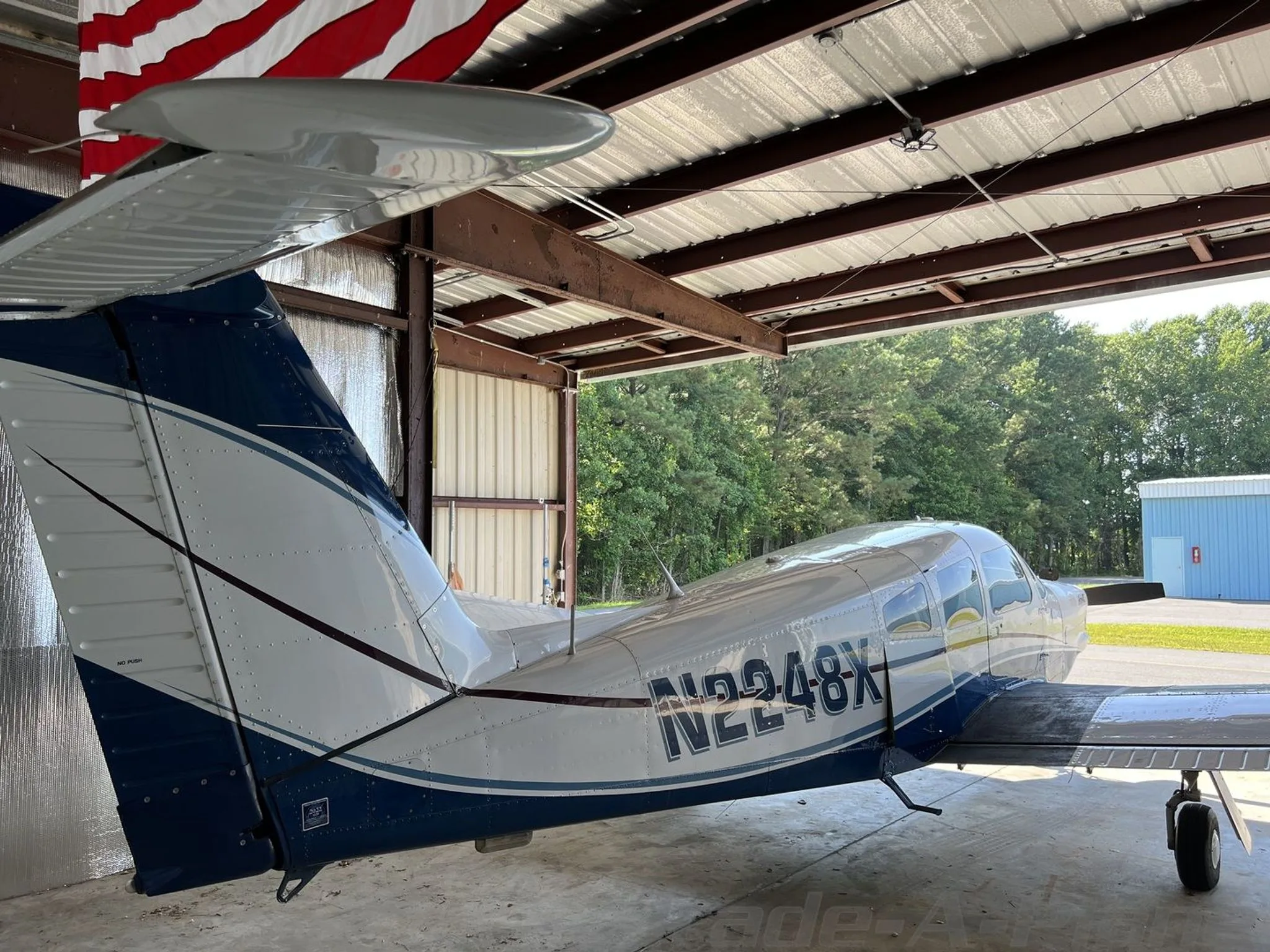 A close-up view of the tail section of a white and blue Piper Archer II (N2248X) inside a hangar.