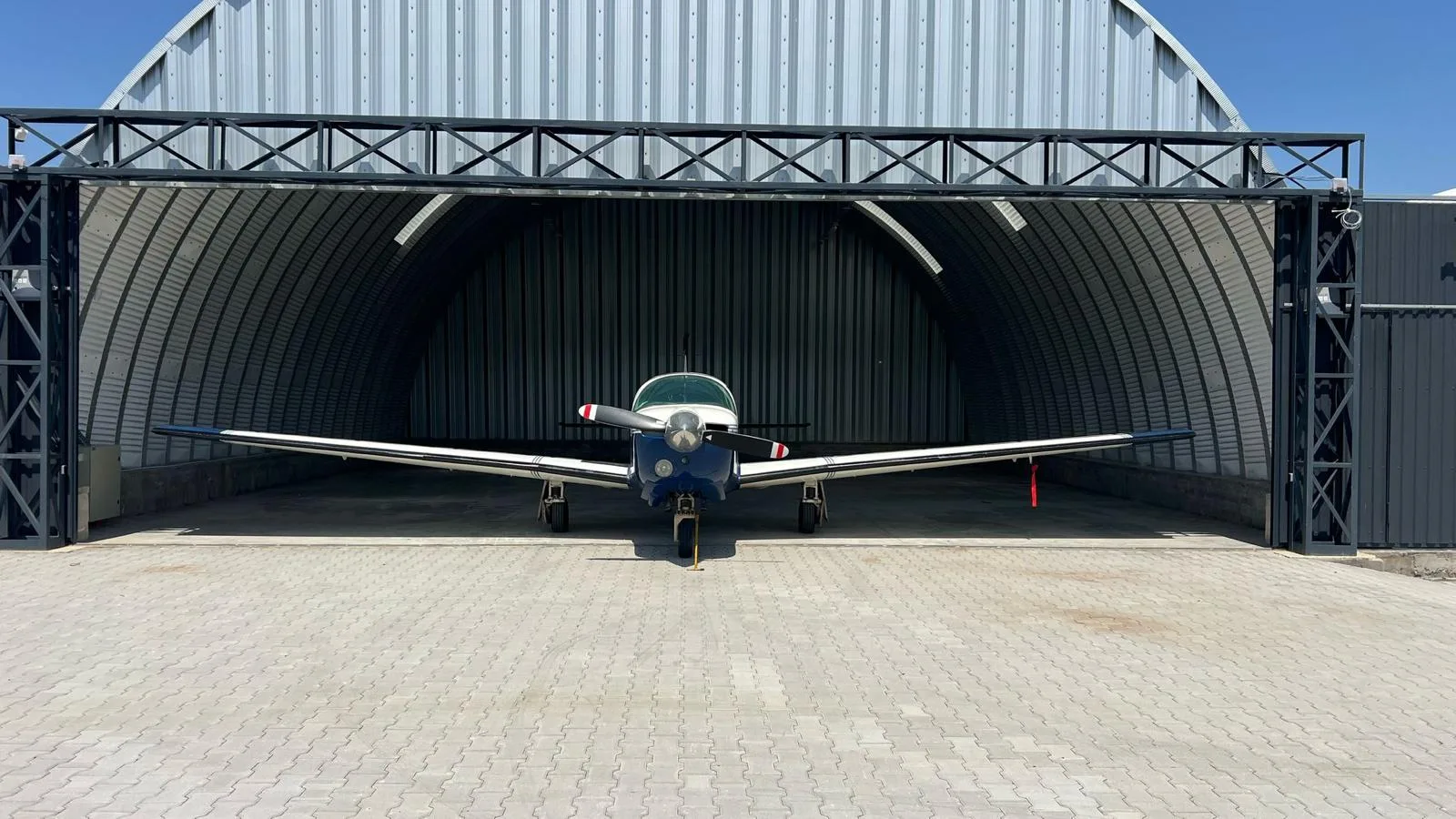 A front view of a blue and white single-engine aircraft parked outside a metal hangar.