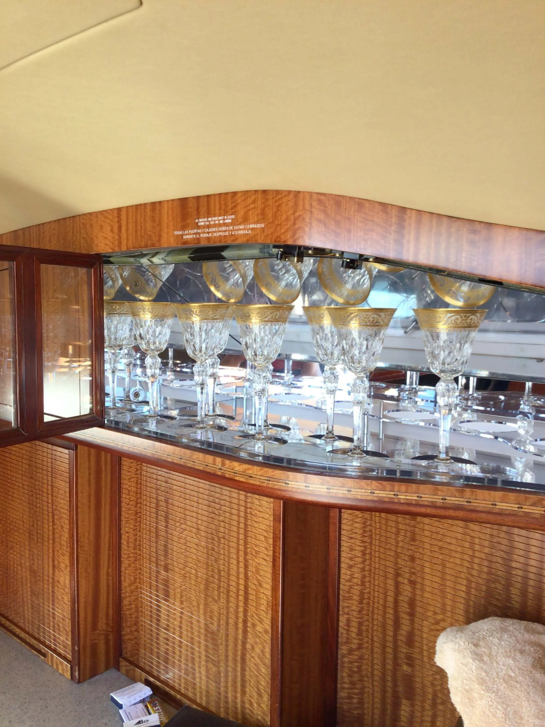 An open cabinet inside an aircraft, revealing a display of ornate crystal glasses with gold rims.