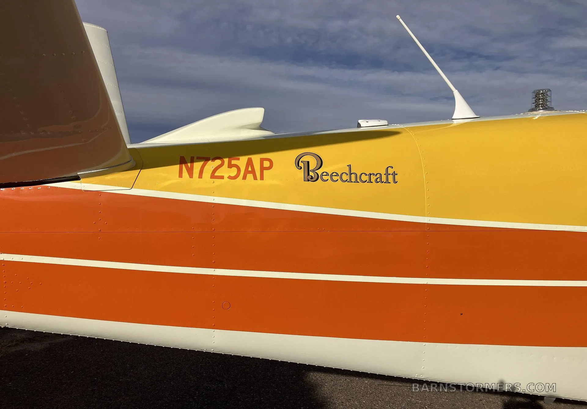 A close-up of the tail section of a white, orange, and yellow Beechcraft Bonanza N725AP, showing the N-number and "Beechcraft" logo.