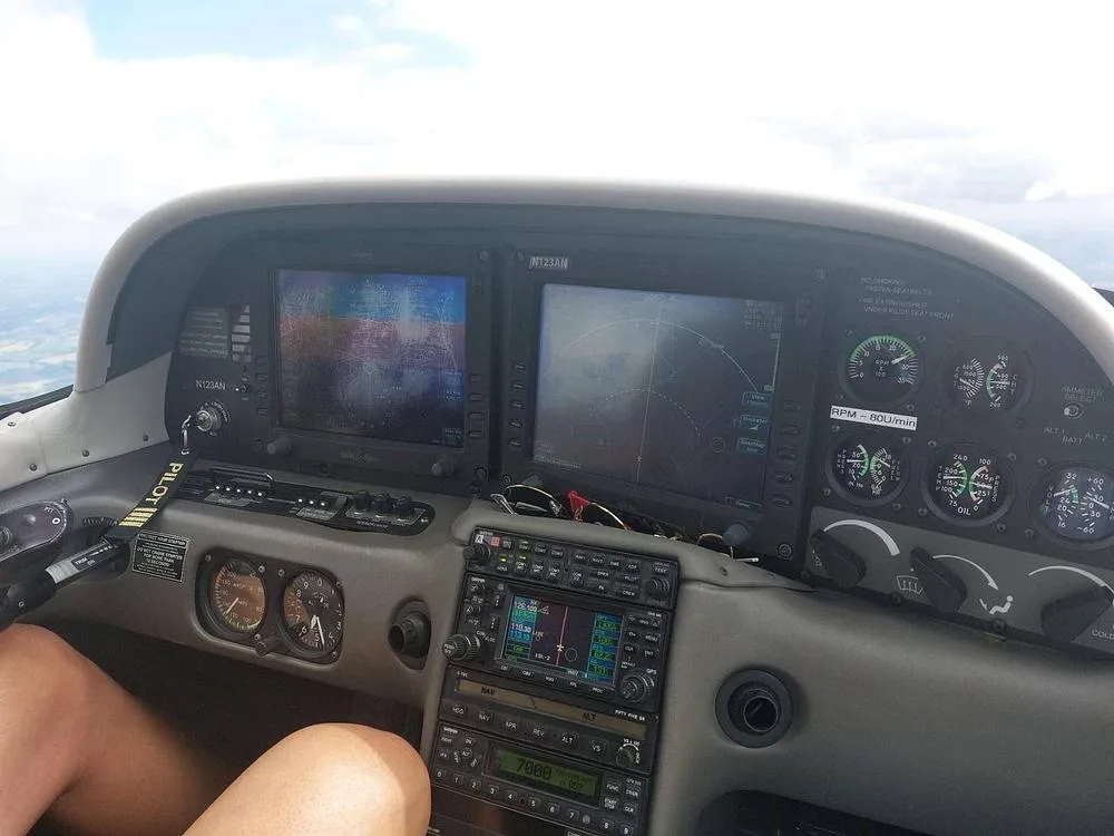 The cockpit of an aircraft showing the instrument panel with two large display screens and various gauges.