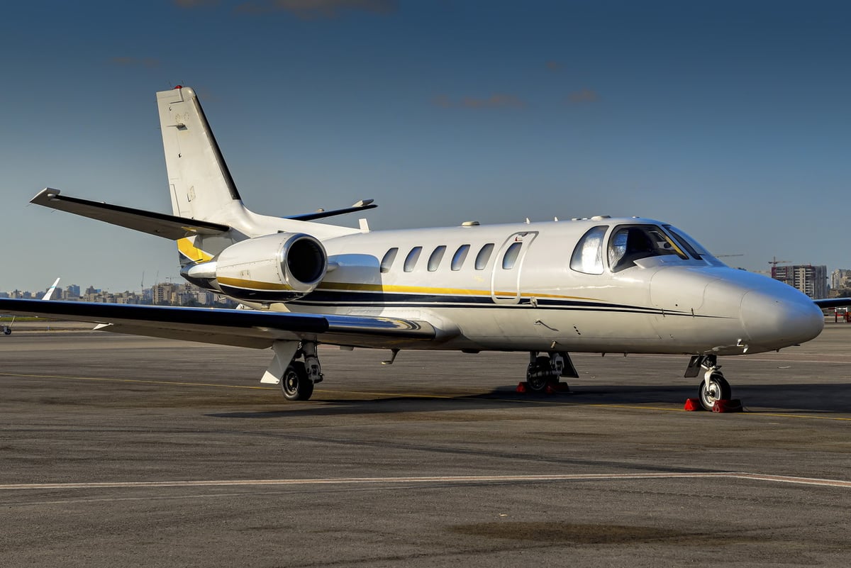 A white jet aircraft parked on the tarmac with a city skyline in the background.