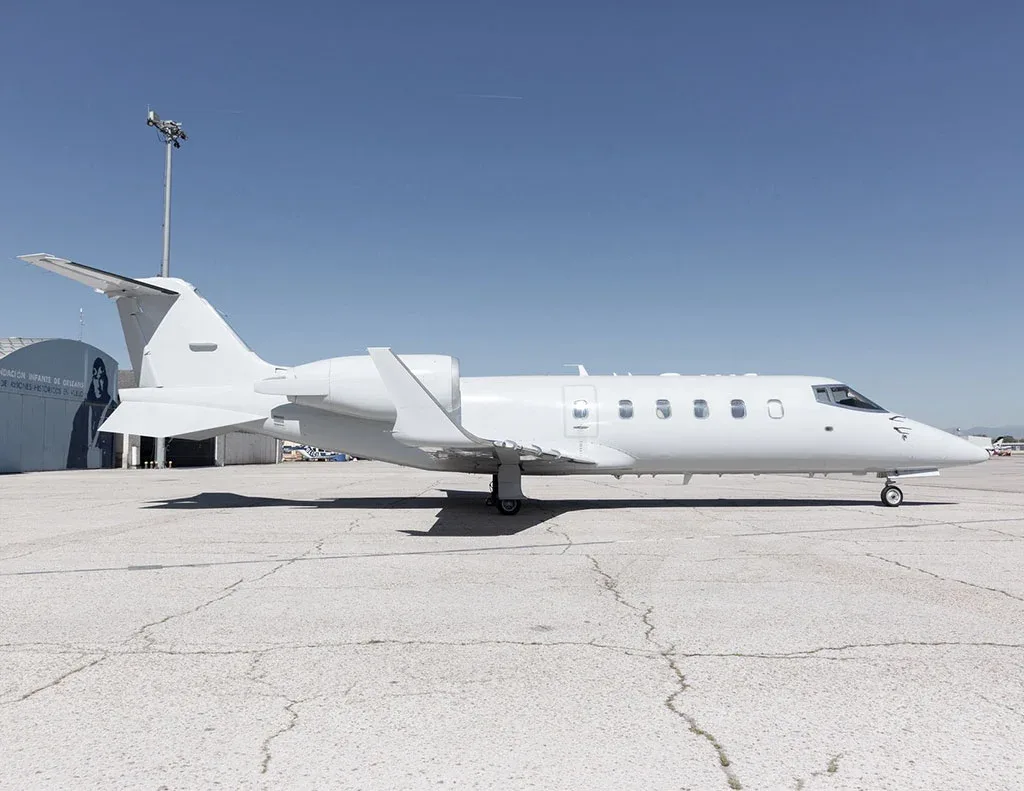 A white Learjet business jet parked on an airport tarmac under a clear blue sky.