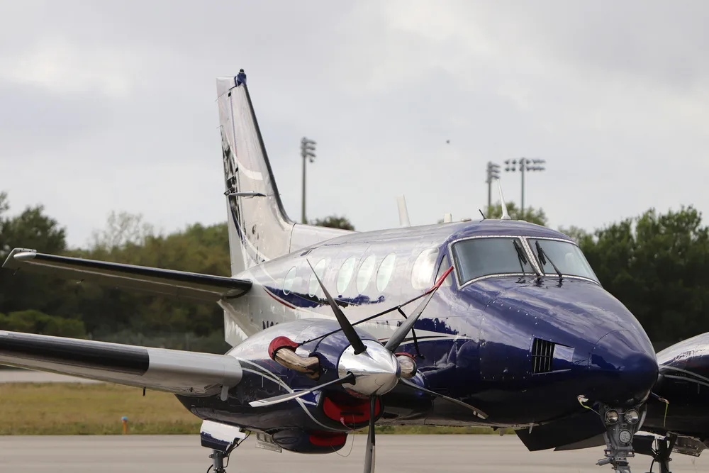 A close-up front-side view of a blue and white twin-engine turboprop aircraft on a tarmac.