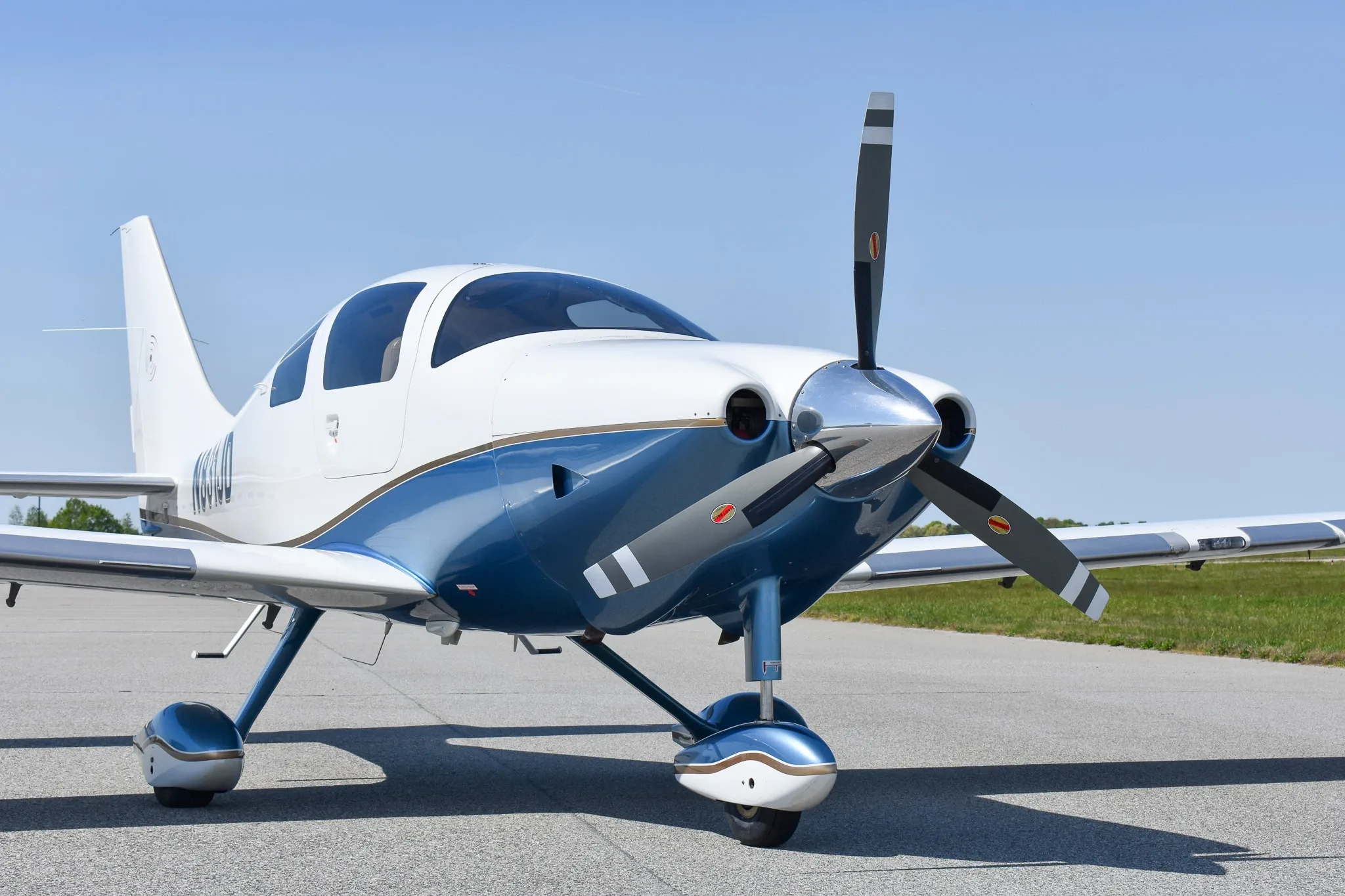 Front view of a white and blue single-engine aircraft with a propeller on an airfield.