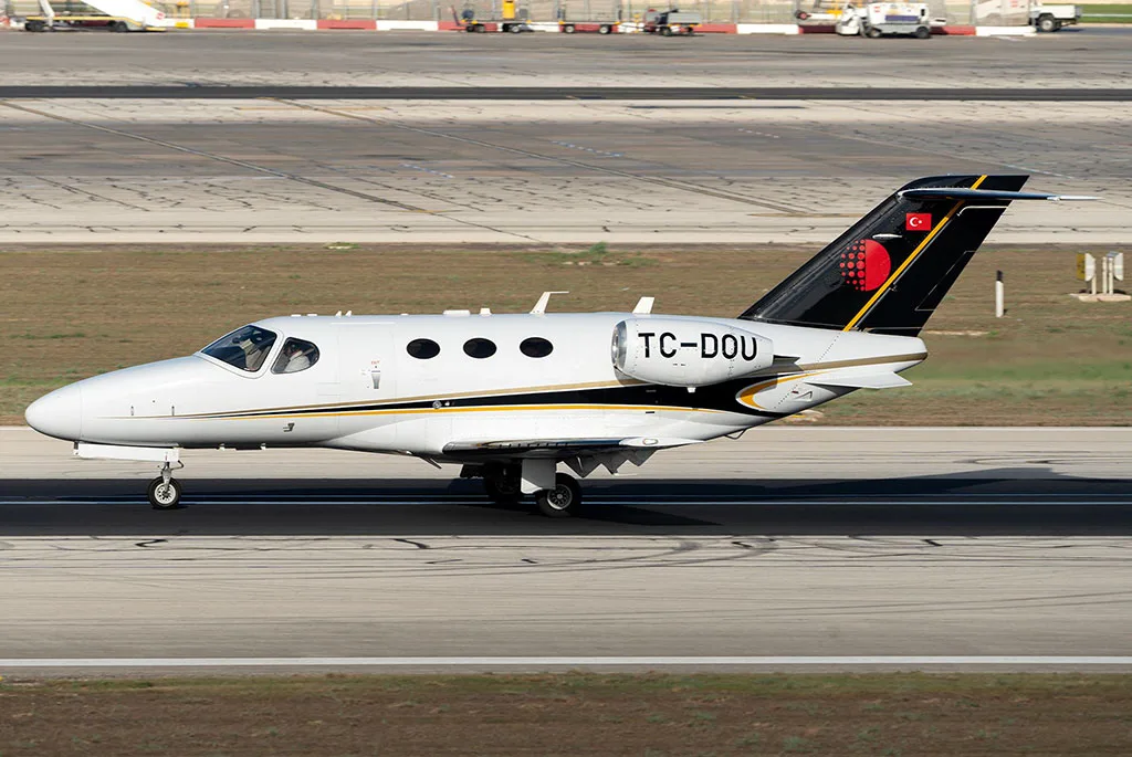 A white business jet with black and gold accents on the tail and fuselage, registration TC-DOU, on a runway or taxiway.