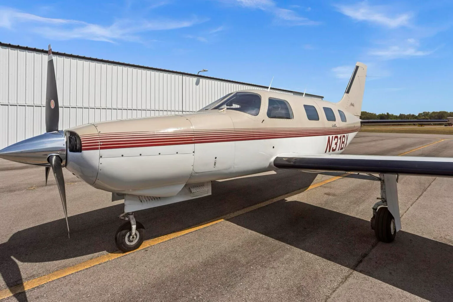 A front-side view of the Piper Malibu N31BX, showing the propeller and nose landing gear on the tarmac.