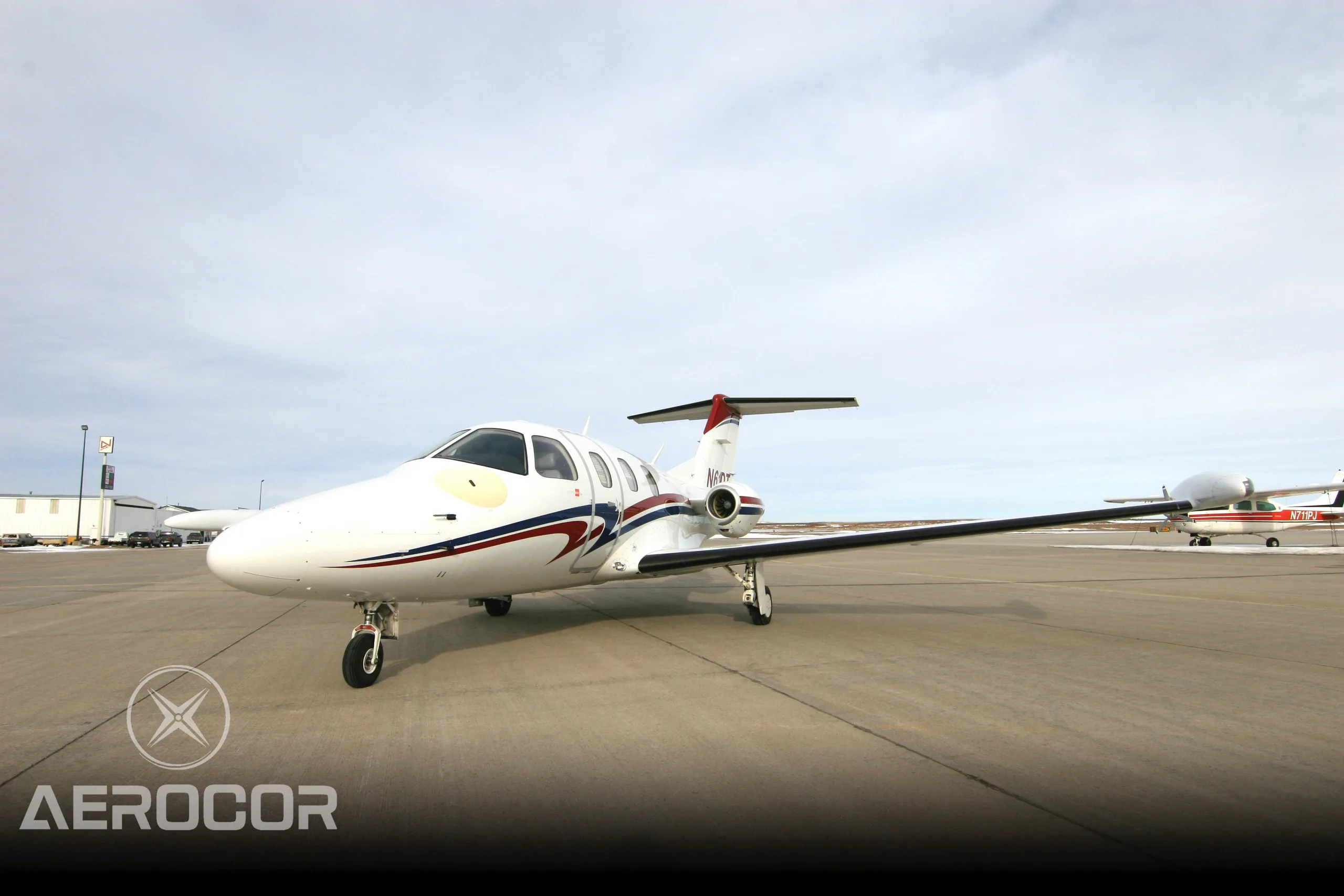 A white Eclipse 500 jet with red and blue stripes on the tarmac, with another aircraft in the background.