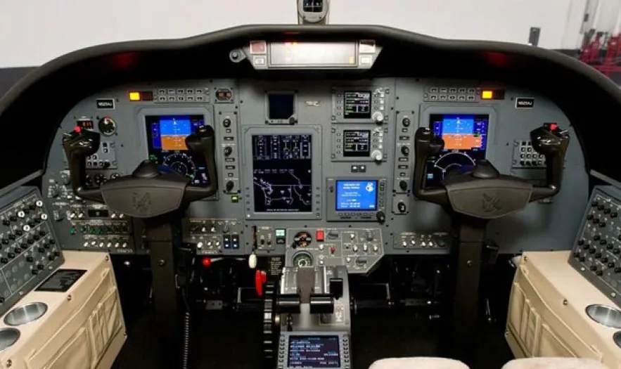 The cockpit of an aircraft featuring multiple digital displays, control yokes, and a central throttle quadrant.