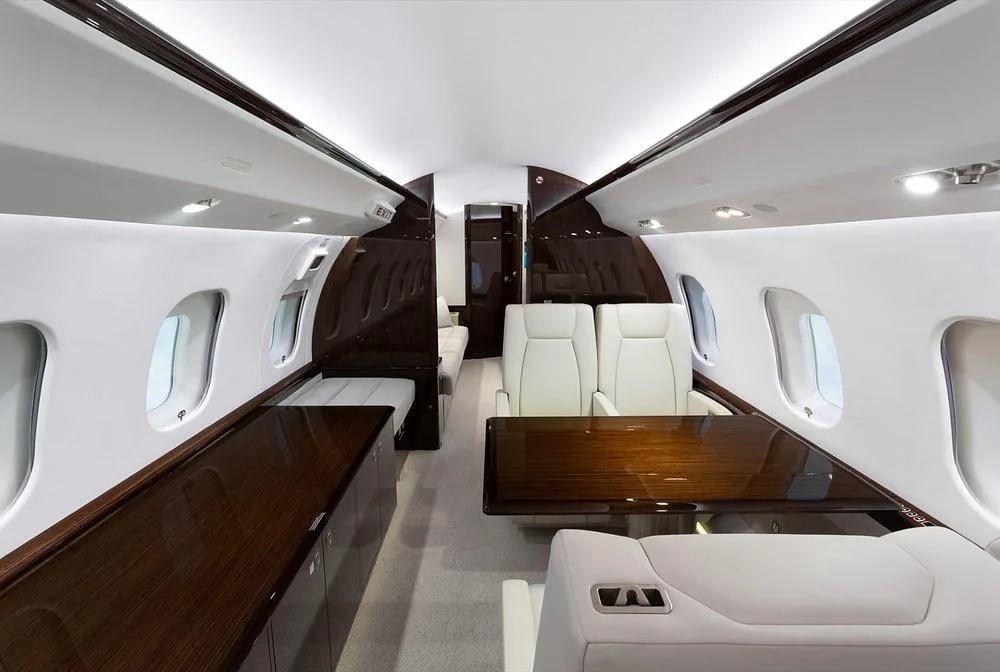 A private jet cabin interior with a large dark wood table, facing seats, and a long credenza along the wall.