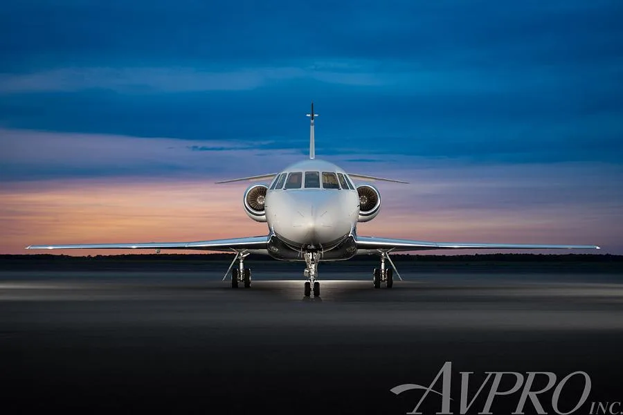 A Dassault Falcon business jet, registration N902AM, seen from the front on an airfield at sunset.