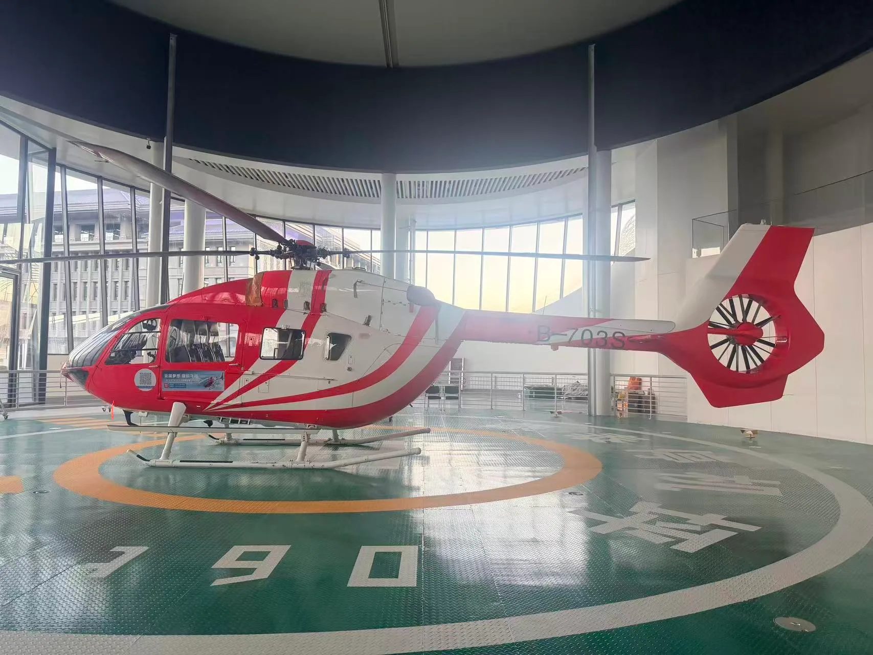 A red and white helicopter is parked on a helipad inside a building.