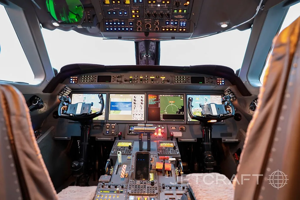 The modern glass cockpit of a business jet with multiple display screens and control yokes.
