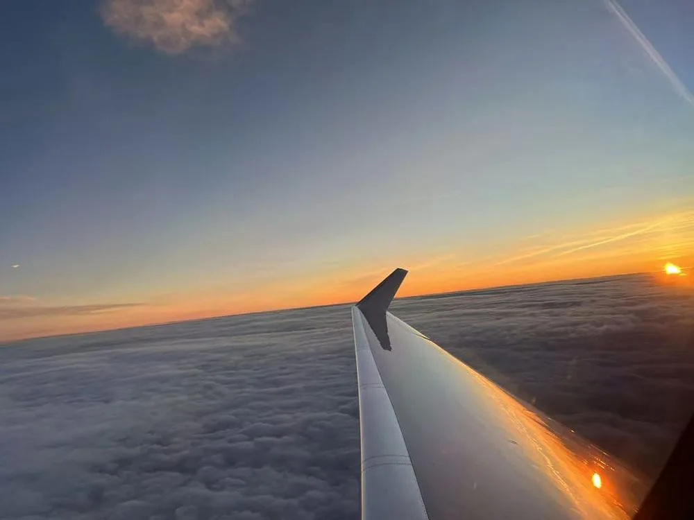 A view from an aircraft window showing the wingtip above clouds during a sunset.