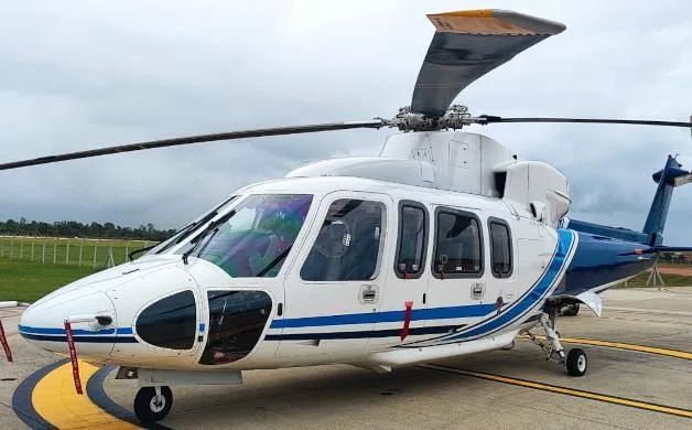 A white and blue AgustaWestland AW139 helicopter is parked on an airport tarmac under a cloudy sky.