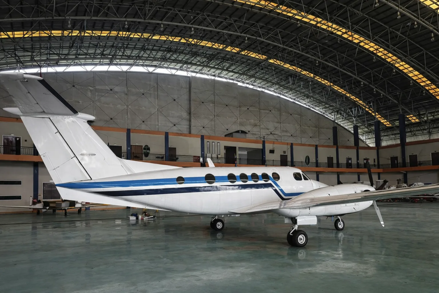 A side view of the white and blue twin-turboprop aircraft, likely a Beechcraft King Air, parked inside a hangar.