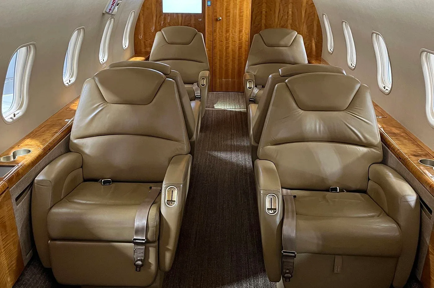 The spacious interior cabin of a business jet featuring tan leather seats arranged in a club configuration.