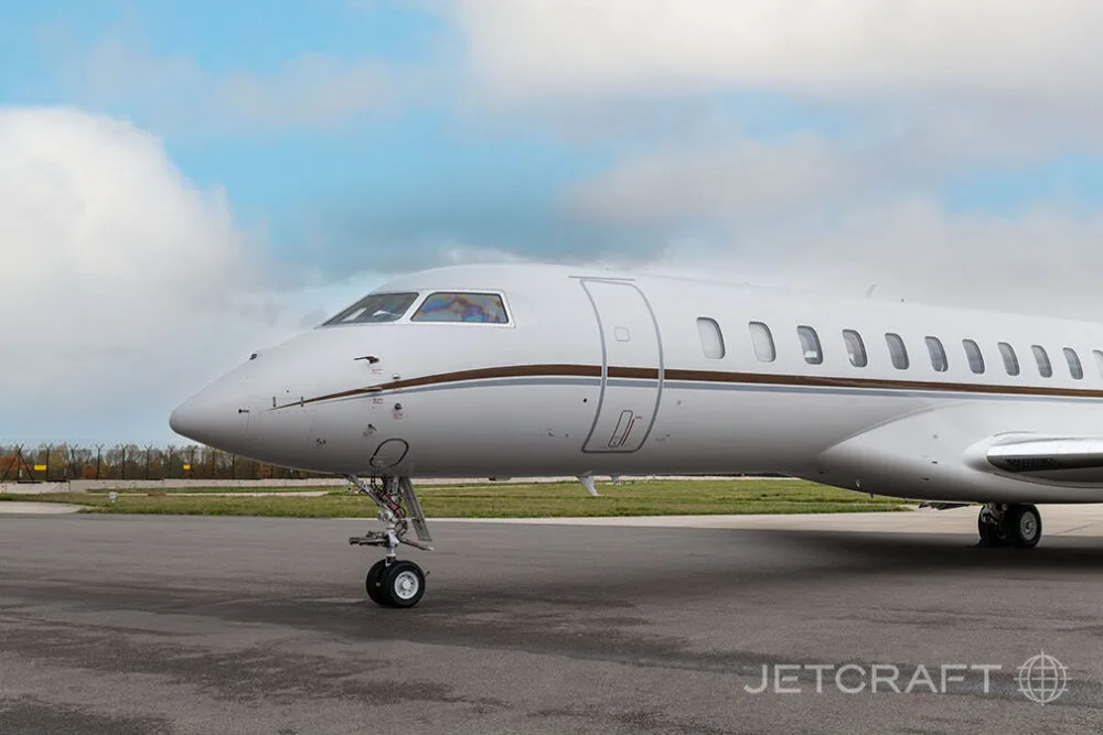 A close-up side view of the nose and front fuselage of a white Bombardier Global business jet on an airfield.