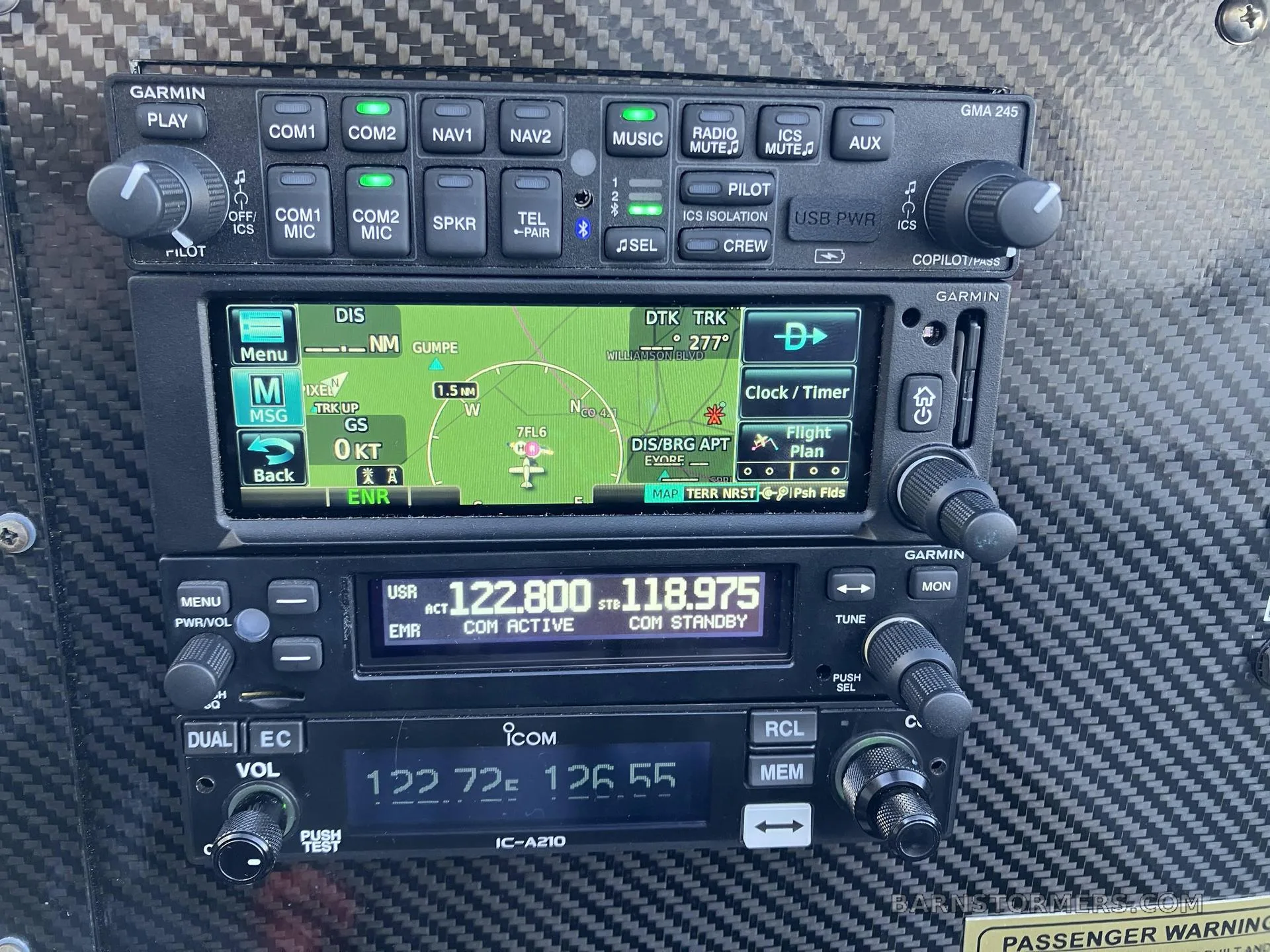 A detailed view of the aircraft's avionics stack, including a Garmin audio panel, GPS/MFD, and Icom radios, set into a carbon fiber panel.