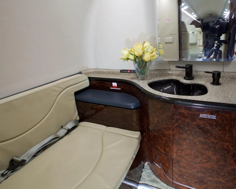 A close-up of the aircraft lavatory with a black sink, dark wood cabinetry, and a vase of yellow roses.