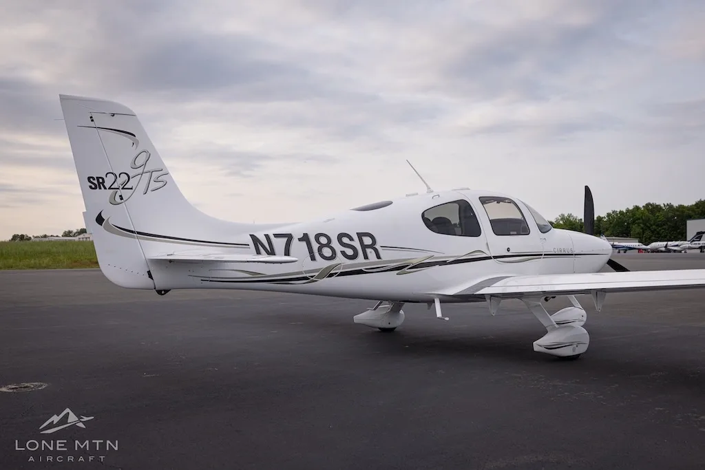 Rear-side view of a white Cirrus SR22T aircraft with black and gold accents parked on an asphalt tarmac.