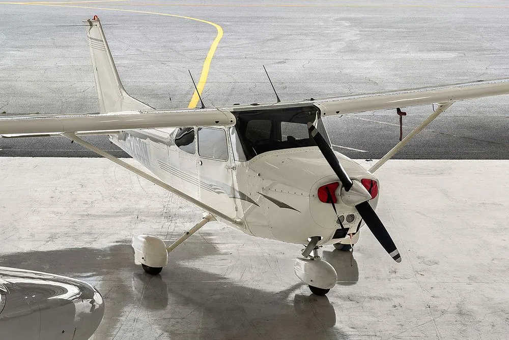 An elevated front-quarter view of the white Cessna 172, registration N5268H, with red propeller covers, on a hangar floor.