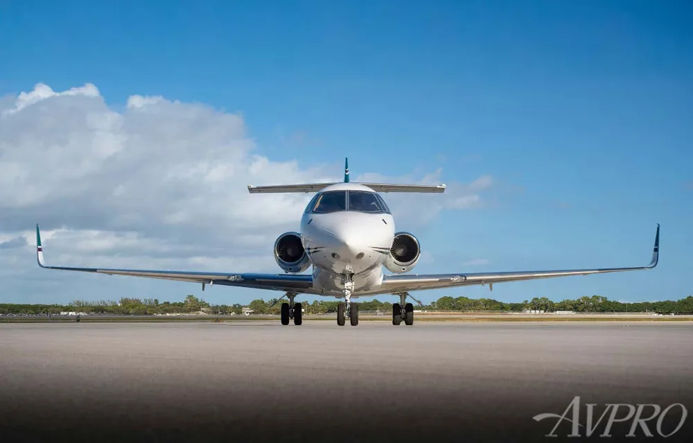 A white and green private jet, N709LP, is viewed head-on on an airfield under a blue sky.