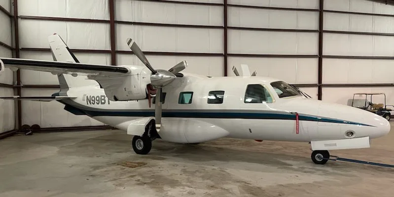 A white twin-engine turboprop aircraft with a blue stripe, registration N99B, parked inside a hangar.