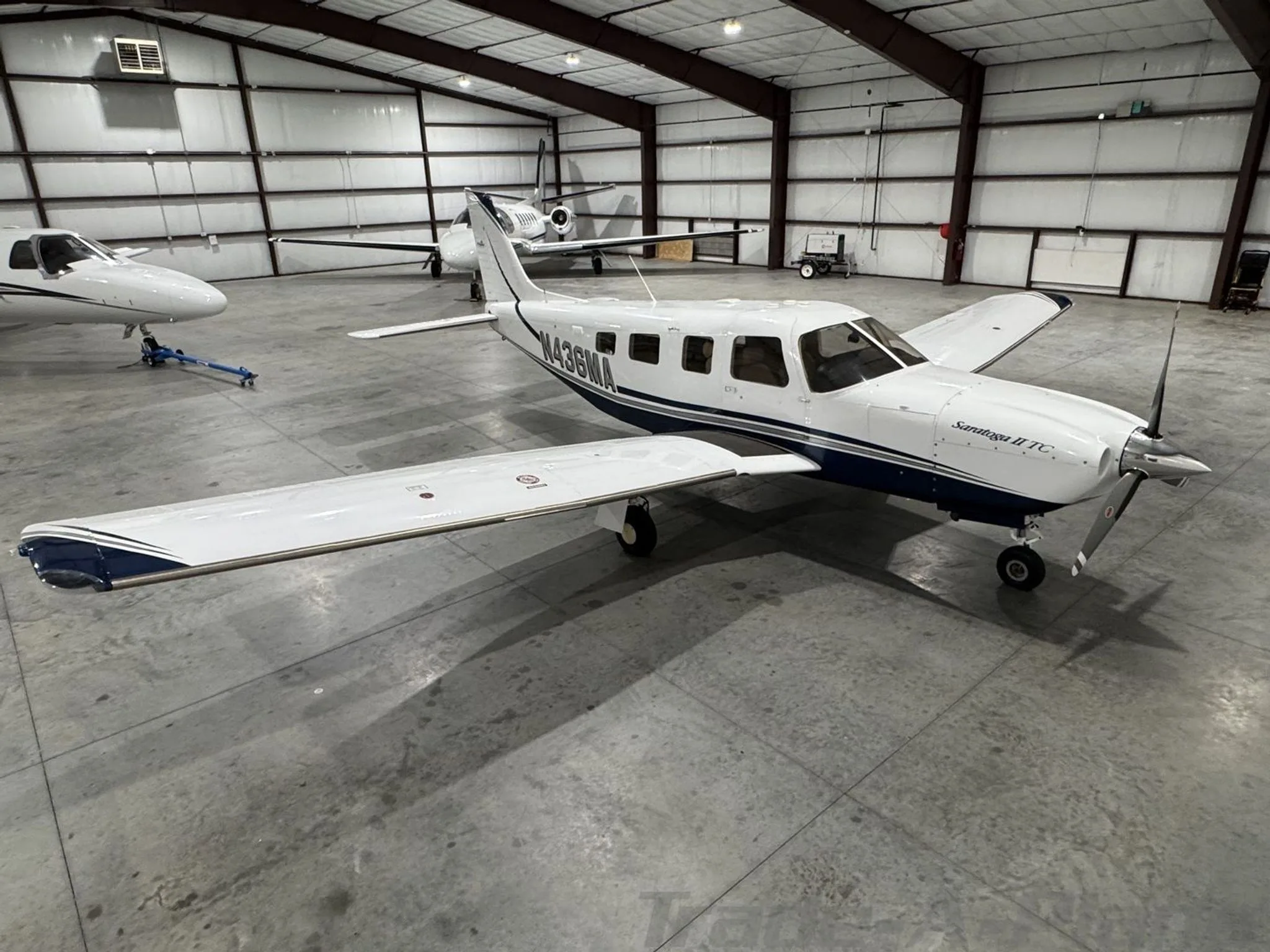 A three-quarter front view of the Piper Saratoga II TC N436MA in a hangar, showing its white and blue paint scheme.