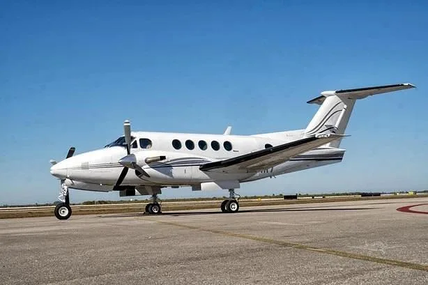 A white Beechcraft King Air 350, registration N124KT, is parked on an airport tarmac under a clear blue sky.