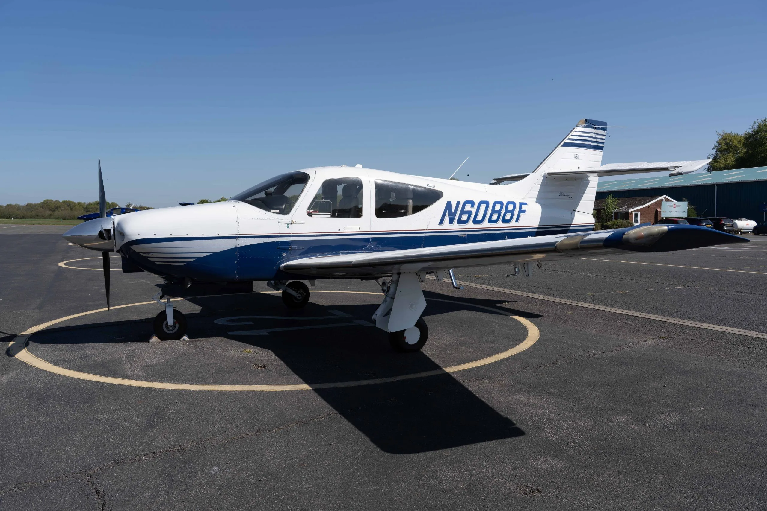 A white and blue Commander 115 aircraft (N6088F) parked on an asphalt tarmac on a sunny day.