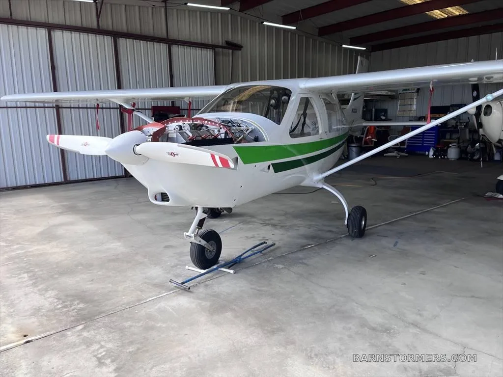 A white and green light aircraft (N333J) with its engine cowling open is parked inside a hangar.