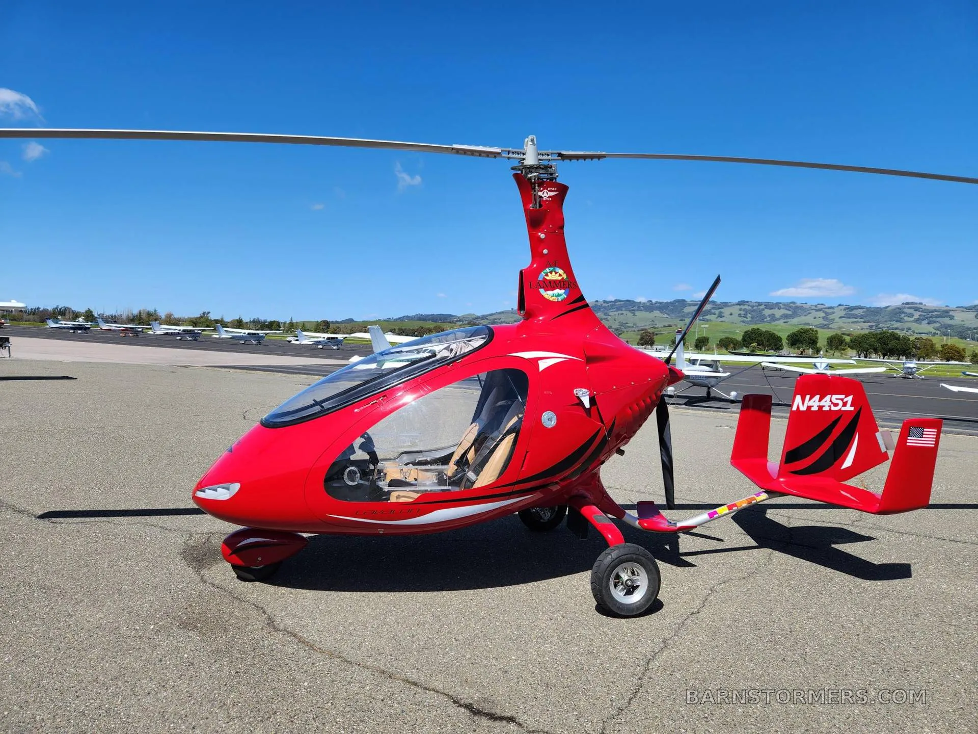 A full side view of the red gyrocopter N4451 parked on an airfield under a clear blue sky.