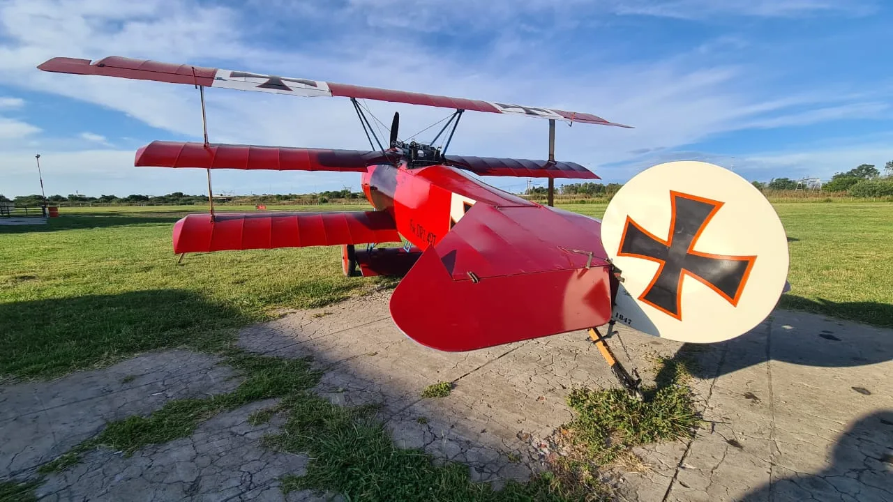 A red Fokker Dr.I replica triplane with German crosses on its wings and tail, parked on a grassy airfield.