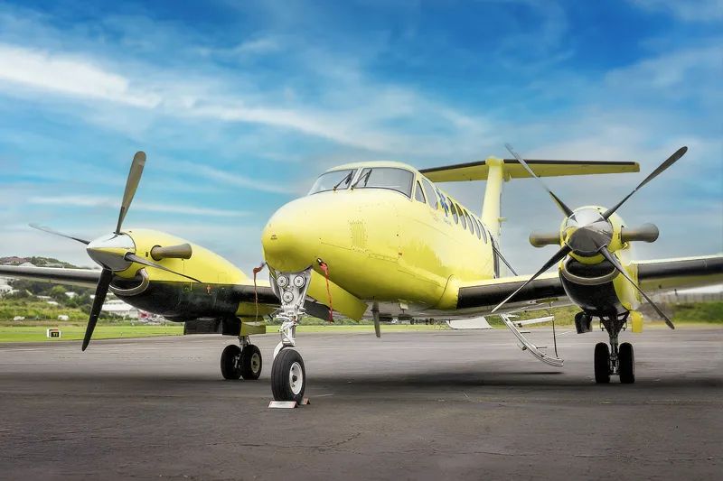 A bright yellow and black twin-engine turboprop aircraft, likely a Beechcraft King Air, parked on an asphalt runway under a blue sky.