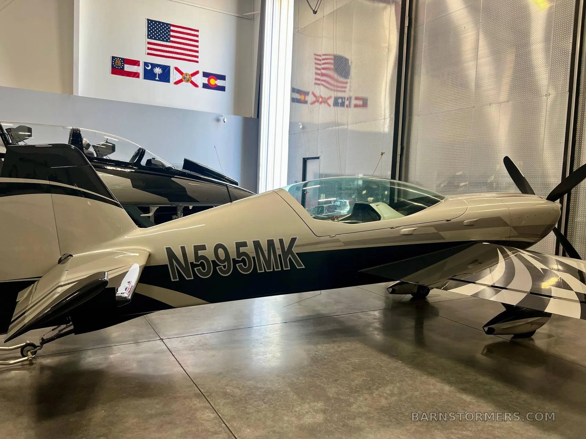 A close-up side view of the silver and black propeller aircraft, registration N595MK, showing its wing design in a hangar.