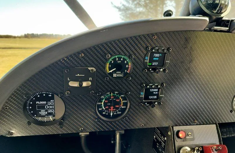 A close-up view of a light sport aircraft's carbon fiber instrument panel, showing flight instruments and engine gauges.