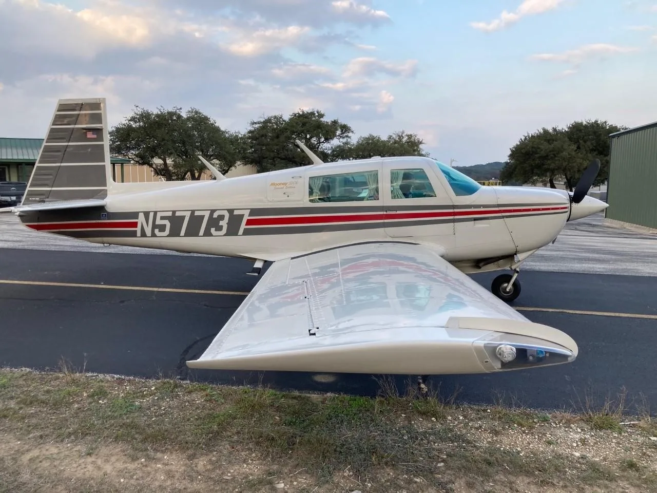A white Mooney 201 aircraft with red and grey stripes, registration N57737, parked on an asphalt ramp.
