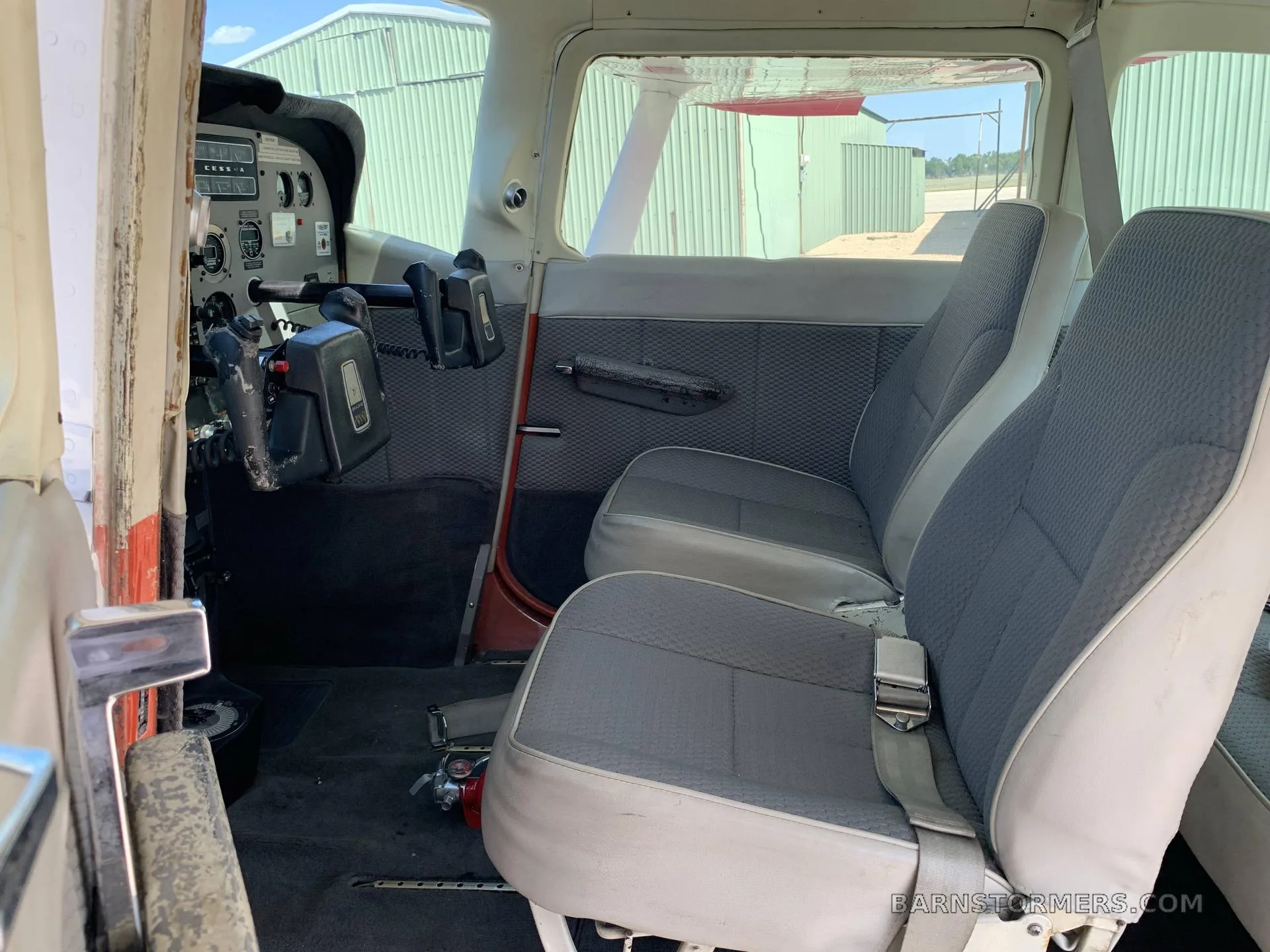 View of the gray and white fabric interior seats in a Cessna aircraft cabin, with the cockpit visible in the foreground.