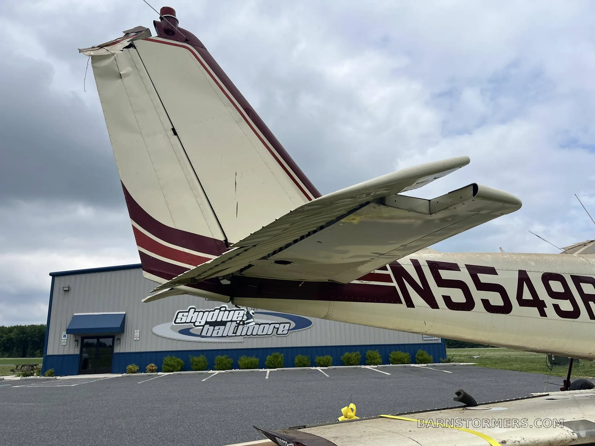 A close-up view of the white and maroon tail section of aircraft N5549R, with a "Skydive Baltimore" hangar in the background.