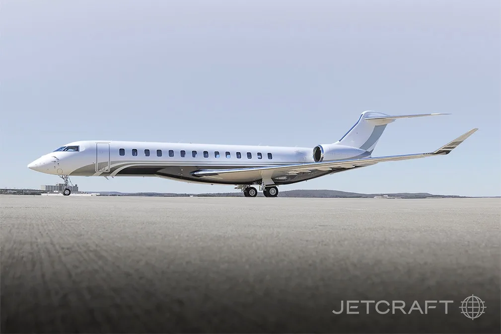A white and grey Bombardier Global 7500 business jet parked on a tarmac under a clear sky.