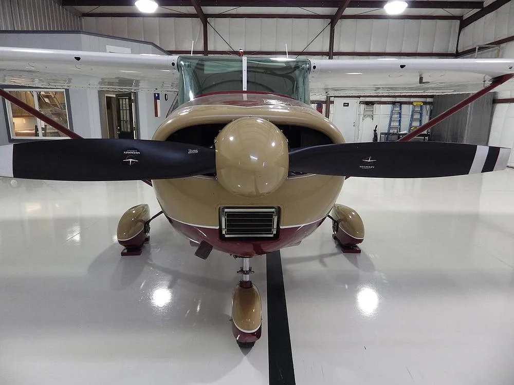 A front view of a red and gold single-engine aircraft with a two-blade propeller, parked in a hangar.