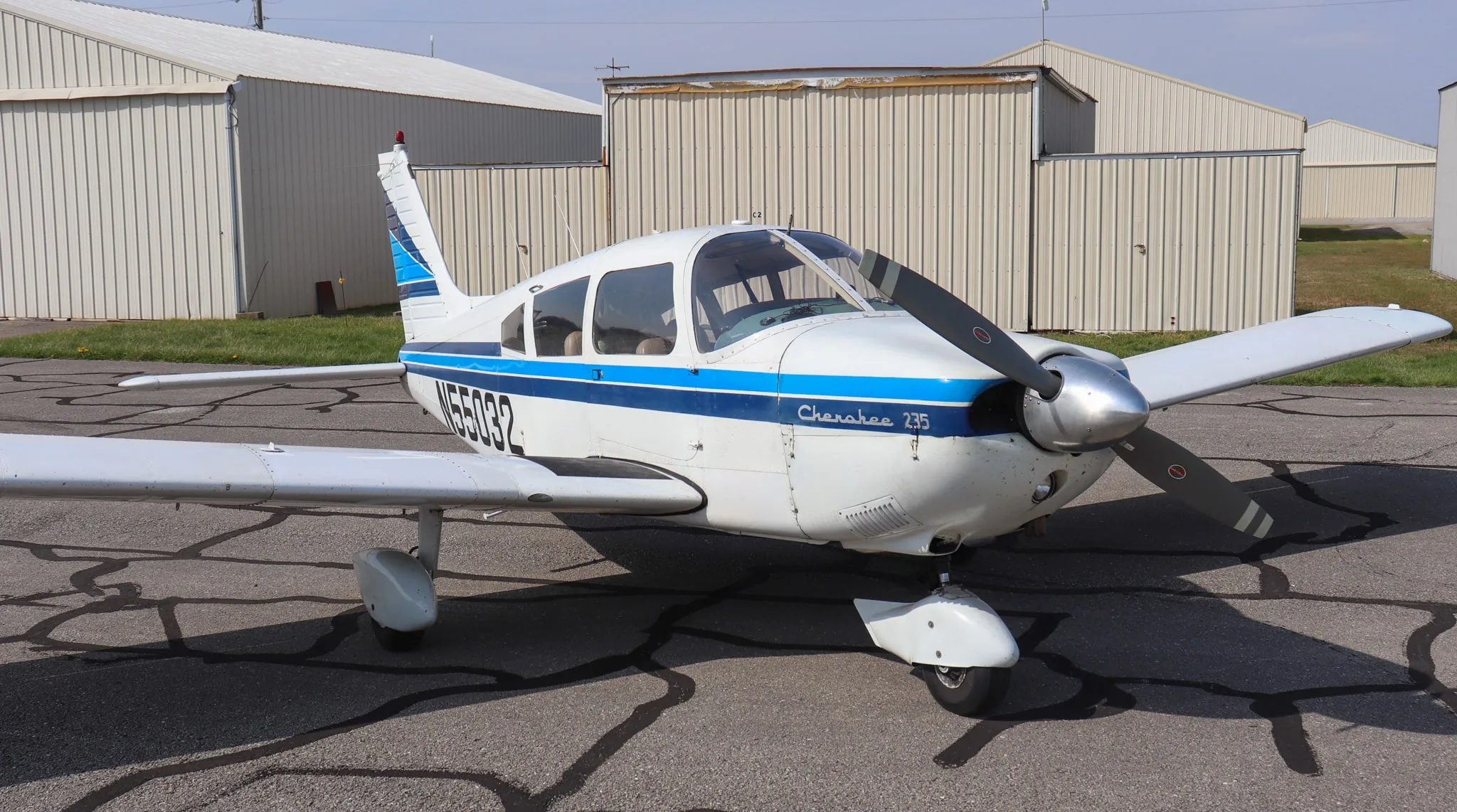 A front-side view of the white Piper Cherokee 235 aircraft with blue stripes and registration N55032, parked on an asphalt ramp.