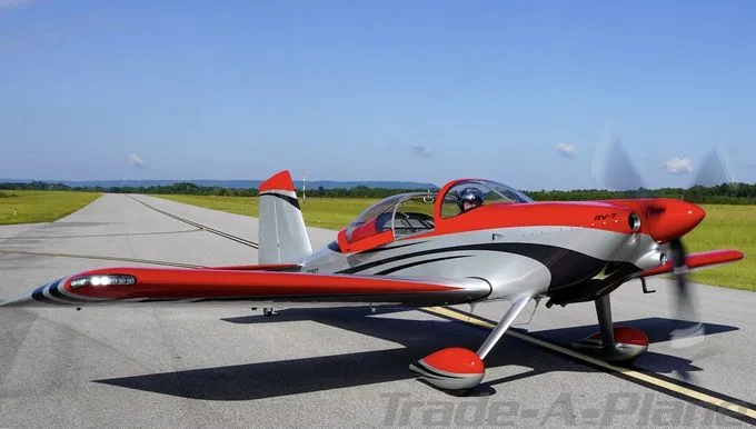 A red and silver Vans RV-7 aircraft with black accents sits on an asphalt runway under a clear blue sky.