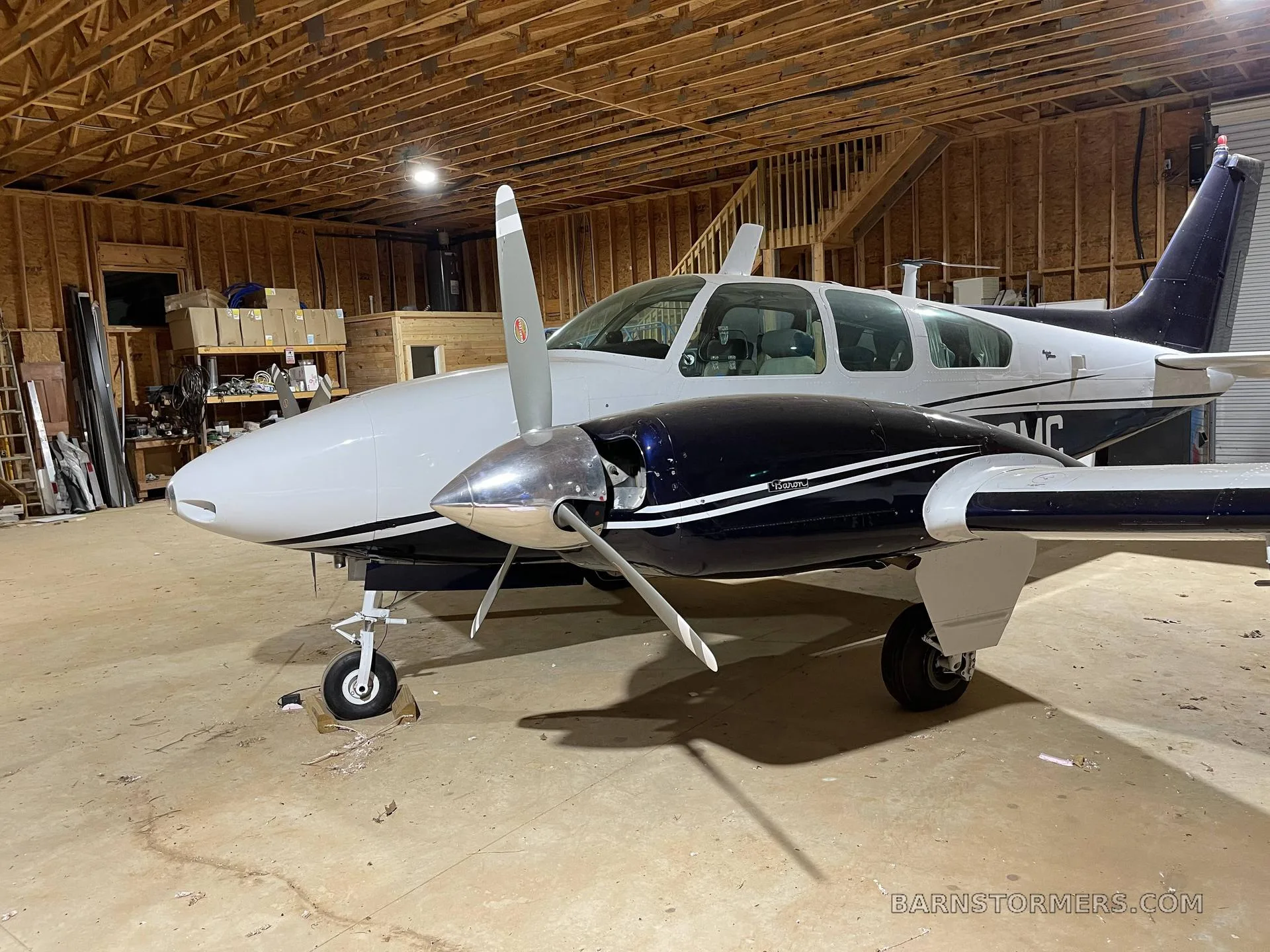 A white and dark blue twin-engine aircraft, N33MG, parked inside a wooden hangar.