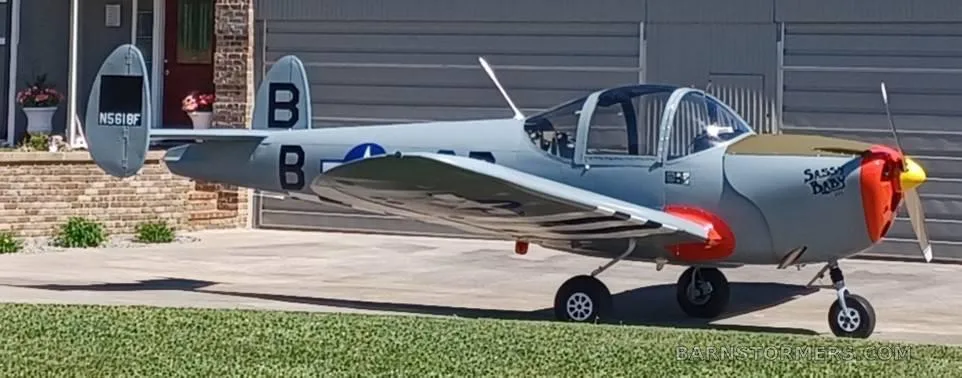 A grey single-engine aircraft with a red nose and "Sassy Baby" text is parked on a concrete driveway.