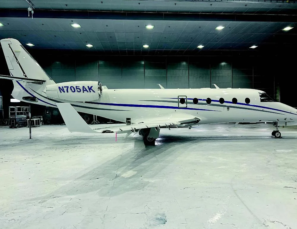 A white business jet, registration N705AK, with blue and grey stripes, parked in a hangar.