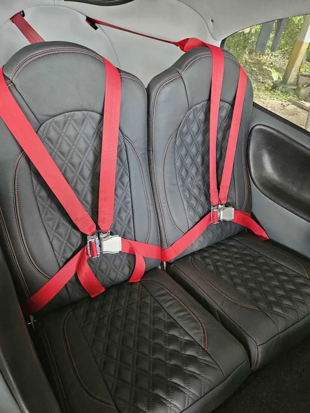 The rear black leather seats with red stitching and red seatbelts inside an aircraft cabin.