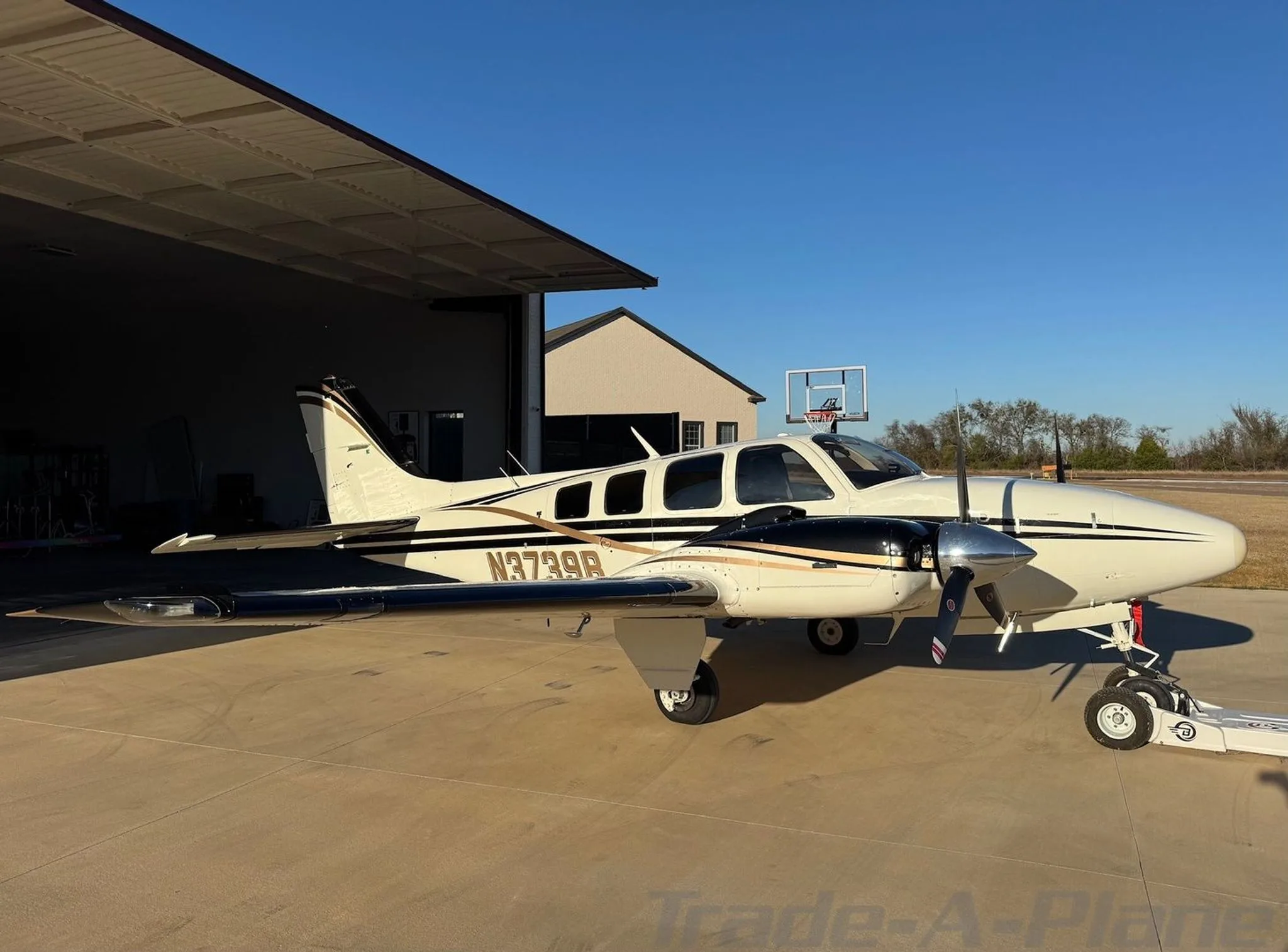 A white and black twin-engine aircraft with gold stripes parked on a tarmac, viewed from the front-right.