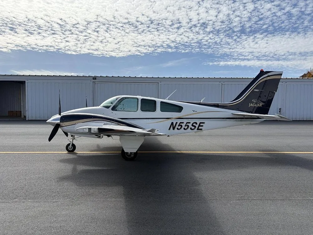 A white and dark blue twin-engine aircraft with registration N55SE is parked on the tarmac, viewed from the left side.